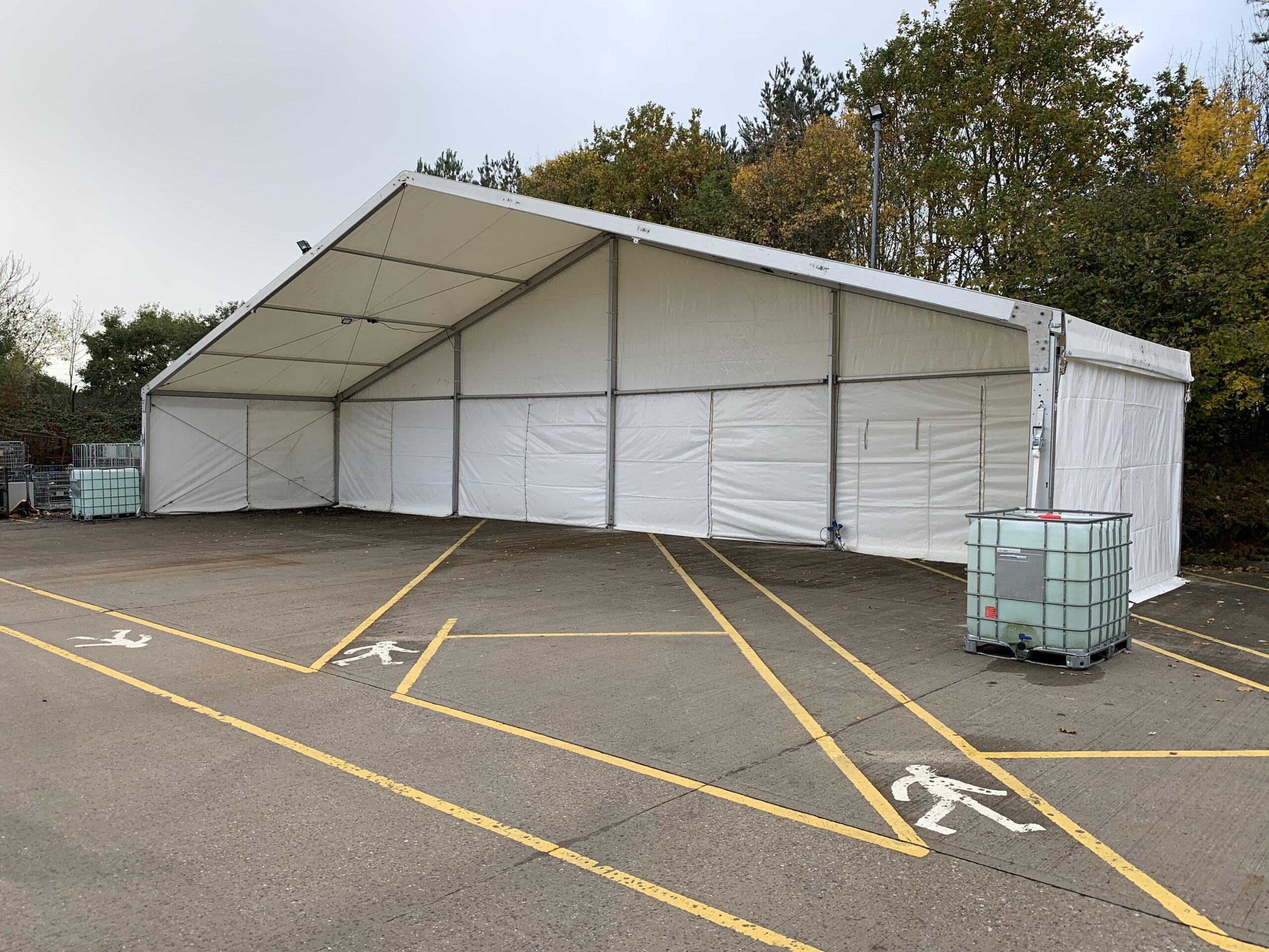 Exterior of a white temporary storage marquee installed in a retail car park with water ballast for stability.
