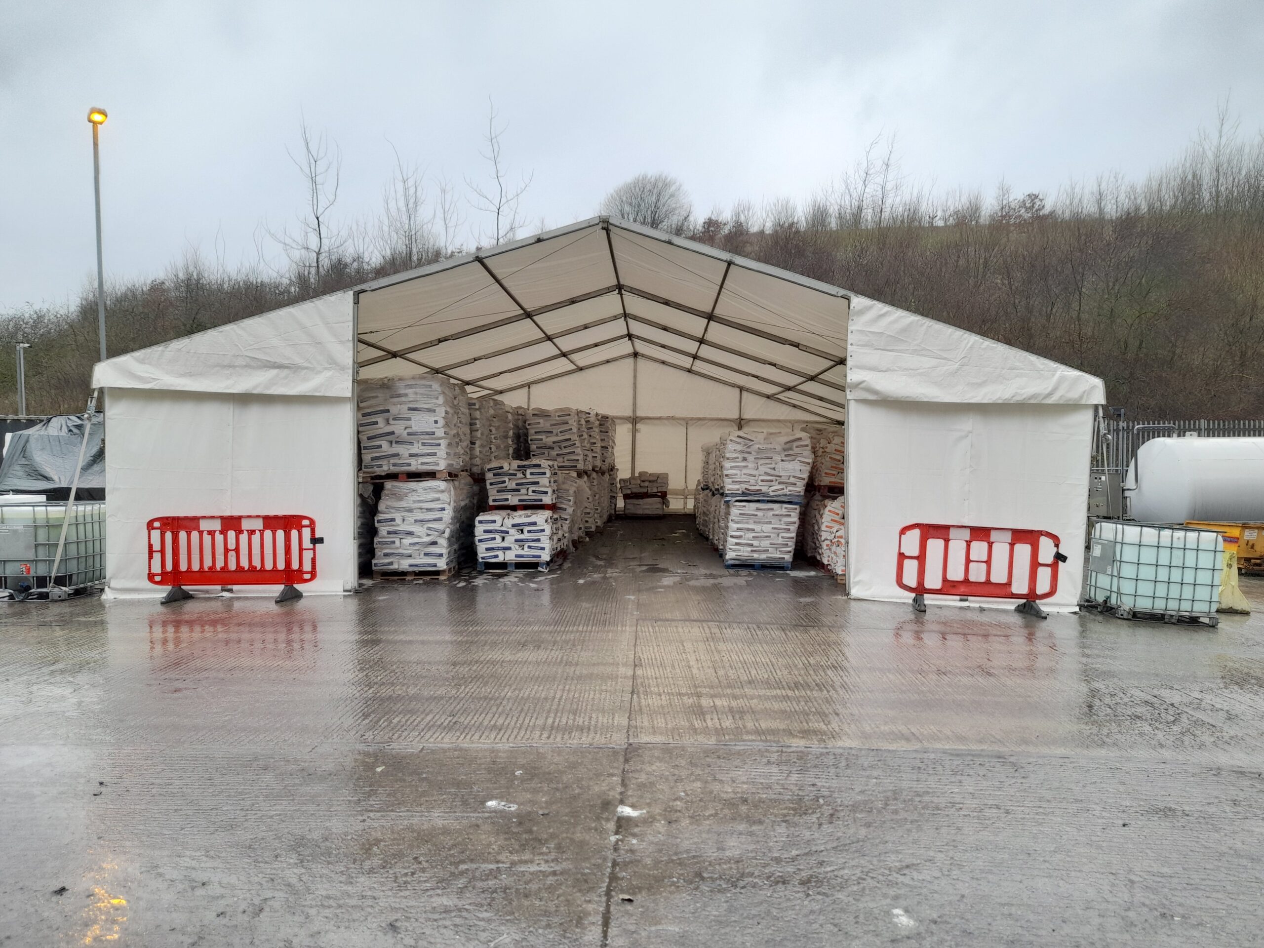 Temporary storage structure housing palletised materials on an industrial site, providing weather-protected storage space.
