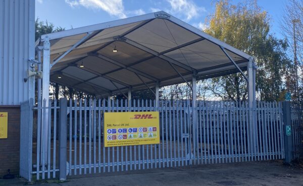 Steel-framed temporary storage structure installed on an industrial site, providing covered operational space behind security fencing.