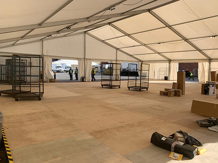 Interior of a temporary storage marquee with hardwood flooring, roll cages and stock handling space at a supermarket site.