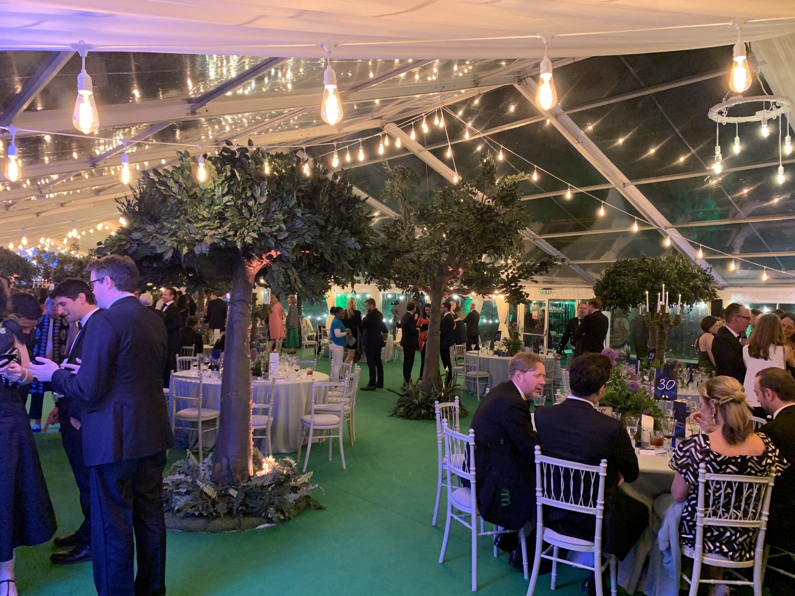 Corporate event marquee interior with dining tables, greenery features and festoon lighting in London