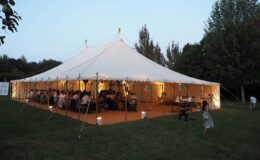 Evening wedding reception inside a traditional canvas pole marquee with warm lighting and wooden flooring in a garden setting