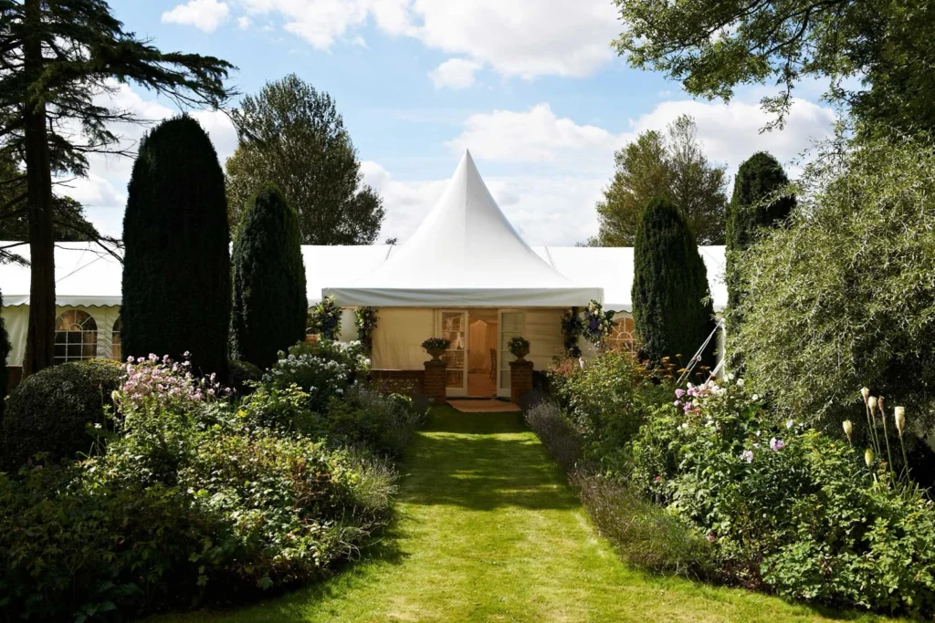 White canvas marquee set within a landscaped garden, surrounded by flowering borders and manicured lawns, ideal for a spring garden party in Hampshire or Surrey.