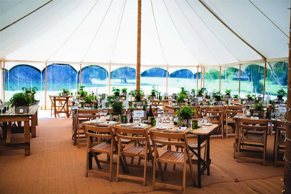 Open-sided pole marquee set for dining with wooden tables and chairs, providing shade for an outdoor event.