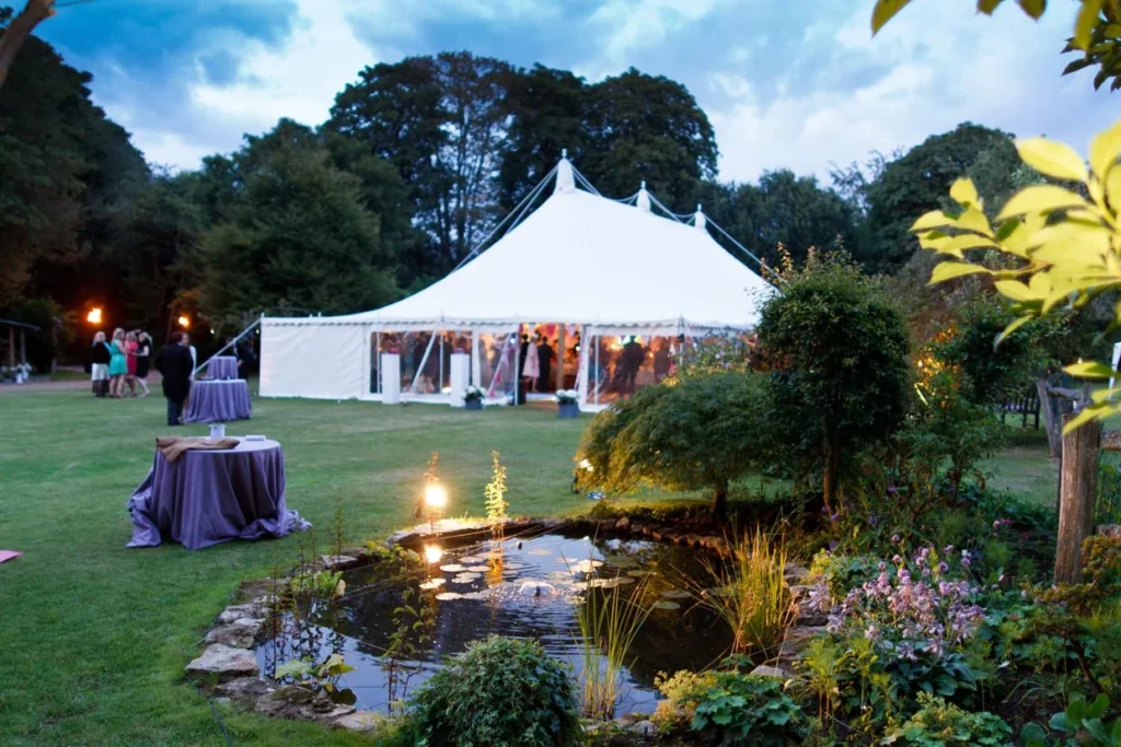 Evening garden event with a white marquee beside a landscaped pond