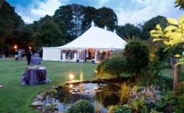Evening garden event with a white marquee beside a landscaped pond
