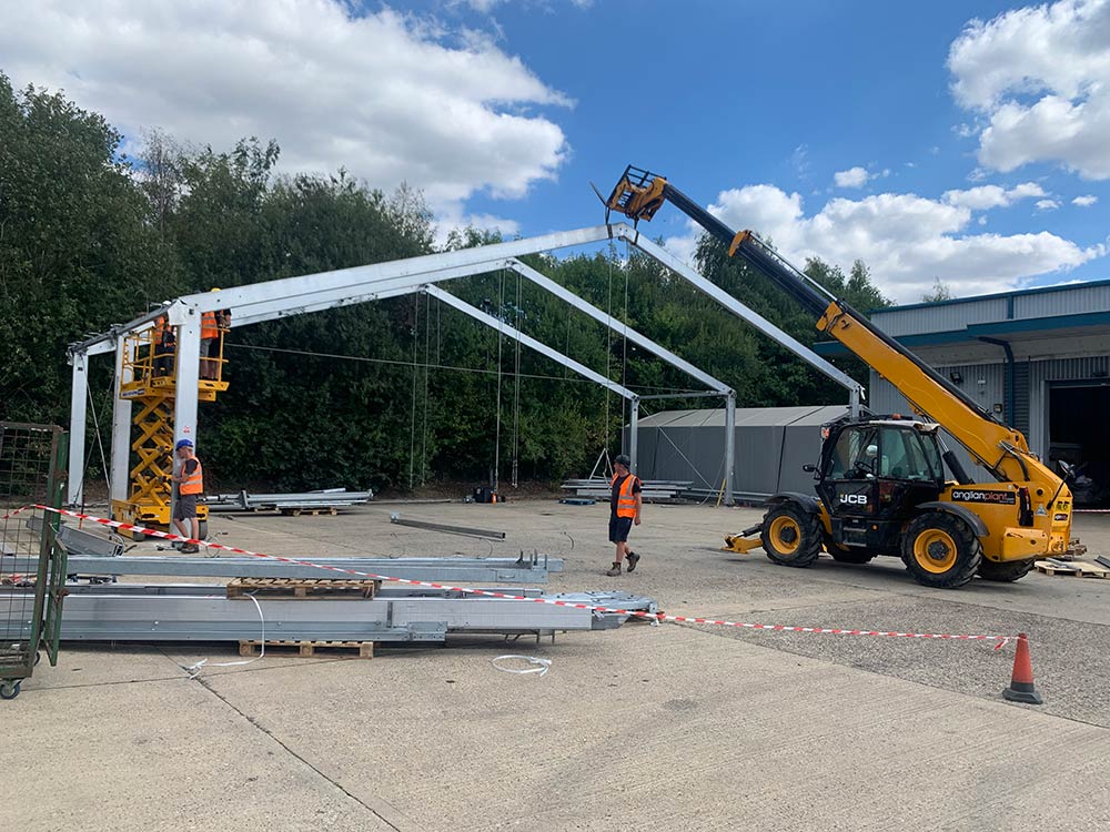 Construction of a temporary storage marquee using a telehandler and steel frame on an industrial site.
