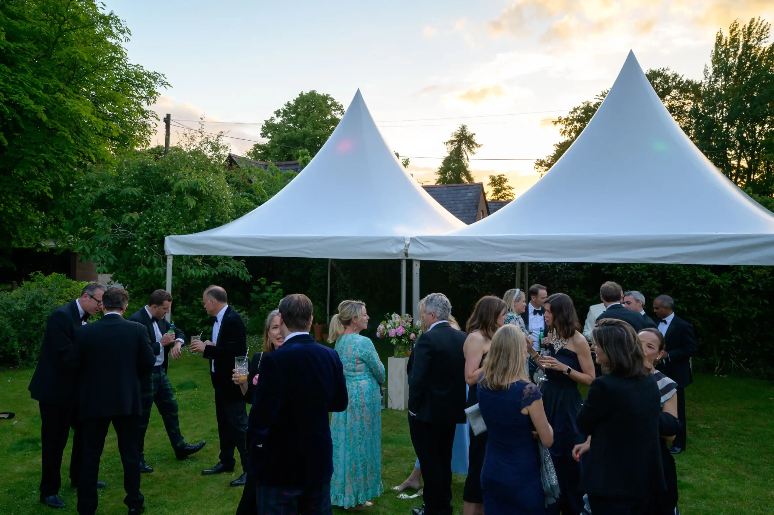Outdoor drinks reception under twin pagoda marquees at sunset with guests in formal attire