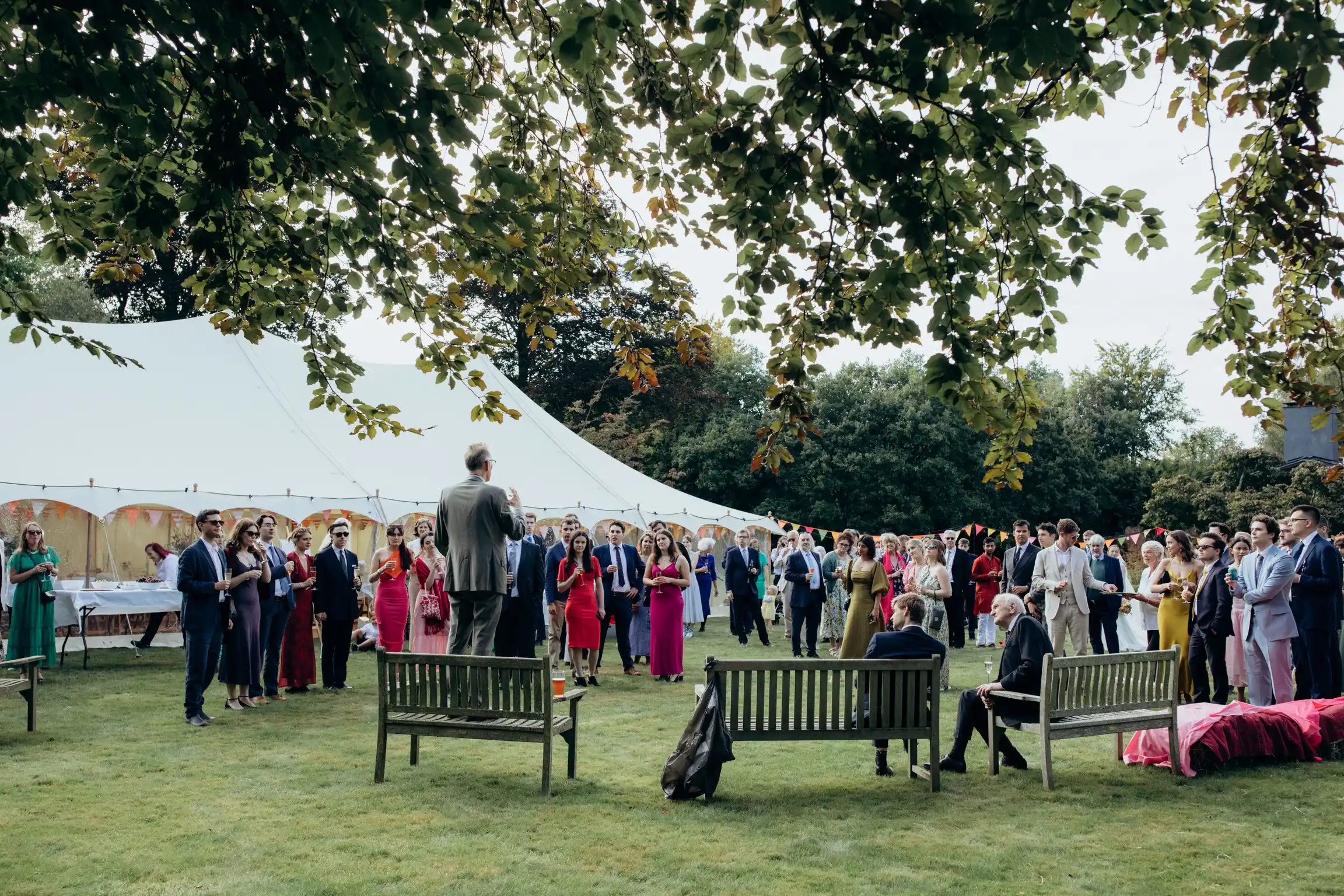 Guests gathered on a lawn outside a large marquee listening to a speech during a summer celebration
