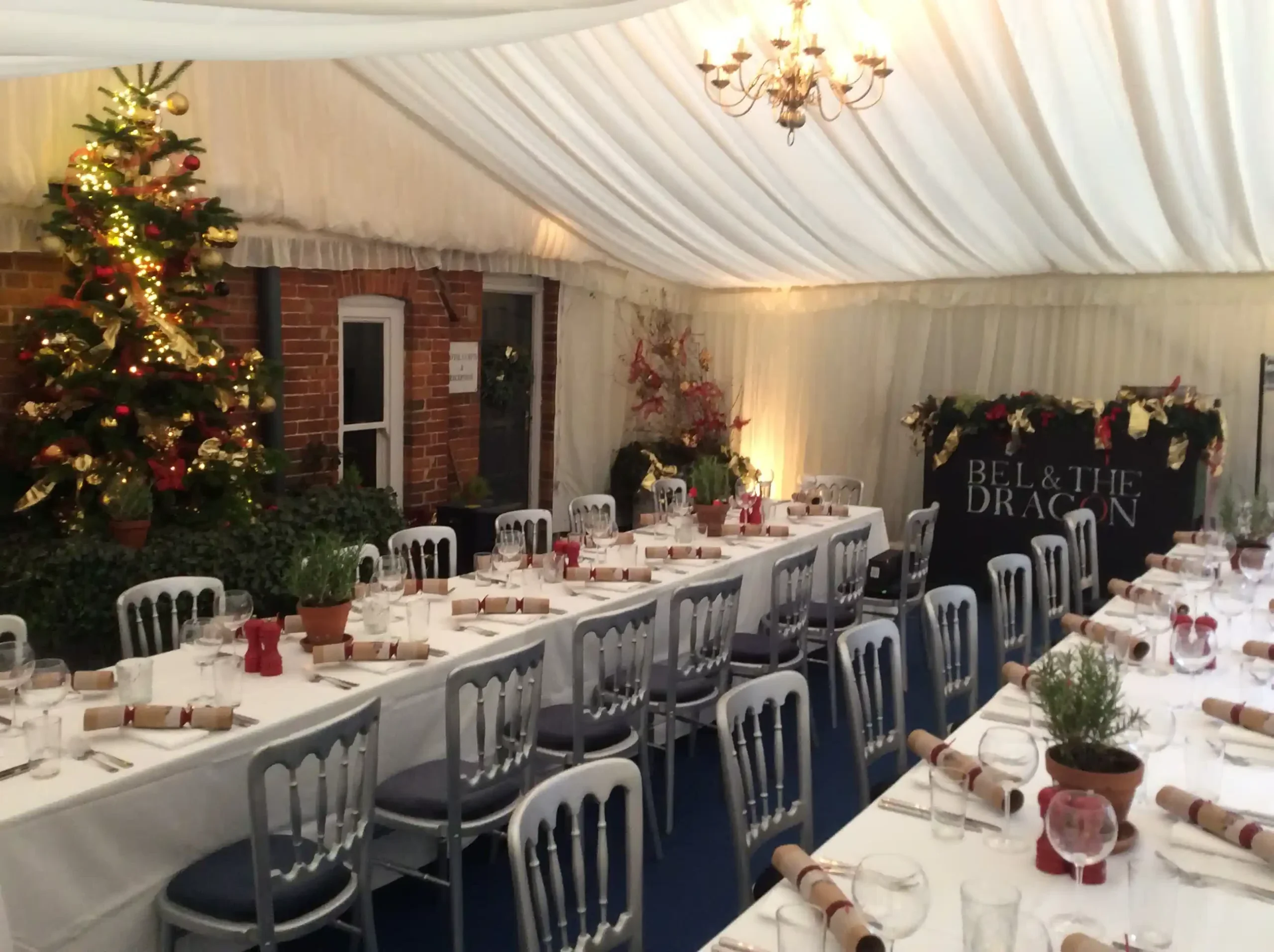 Interior of a Christmas marquee with long dining tables, decorated tree and festive styling at Bel & The Dragon.