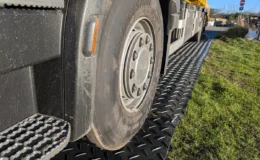 Heavy goods vehicle driving on black HDPE trackway panels laid over grass, demonstrating stable temporary access for large vehicles on soft ground.