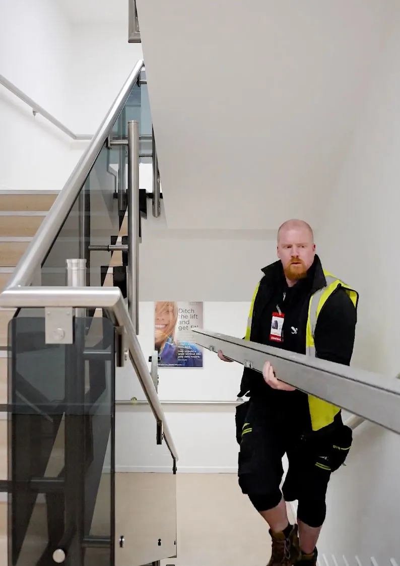 Installation team carrying marquee frame components by hand up stairwell at restricted access London site